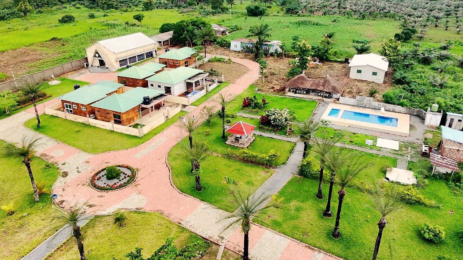 Vue aérienne du centre : chalets, jardins, piscine et allées bordées de palmiers